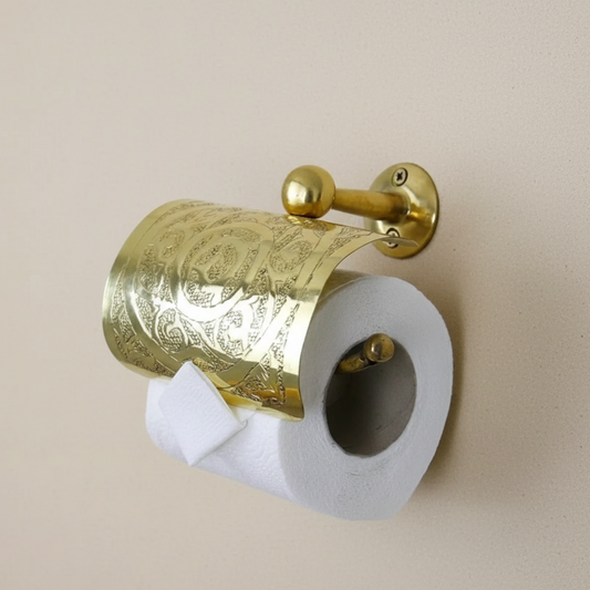 Gold decorative toilet paper holder with a roll of toilet paper on a beige wall.