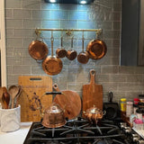 Copper pots and pans hanging above a stove with wooden cutting boards and kitchen utensils.