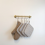 Set of four oven mitts hanging on a gold rack against a white wall