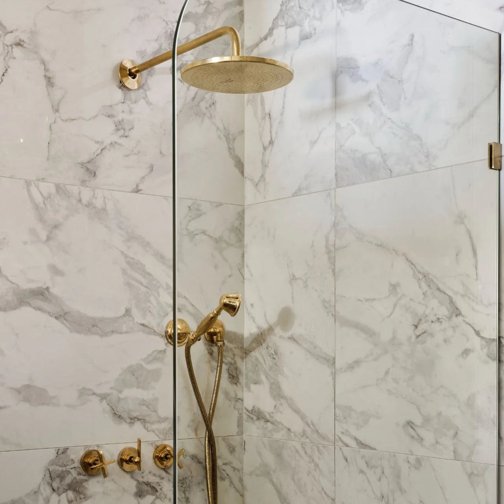 Gold shower head and fixtures on a marble shower wall