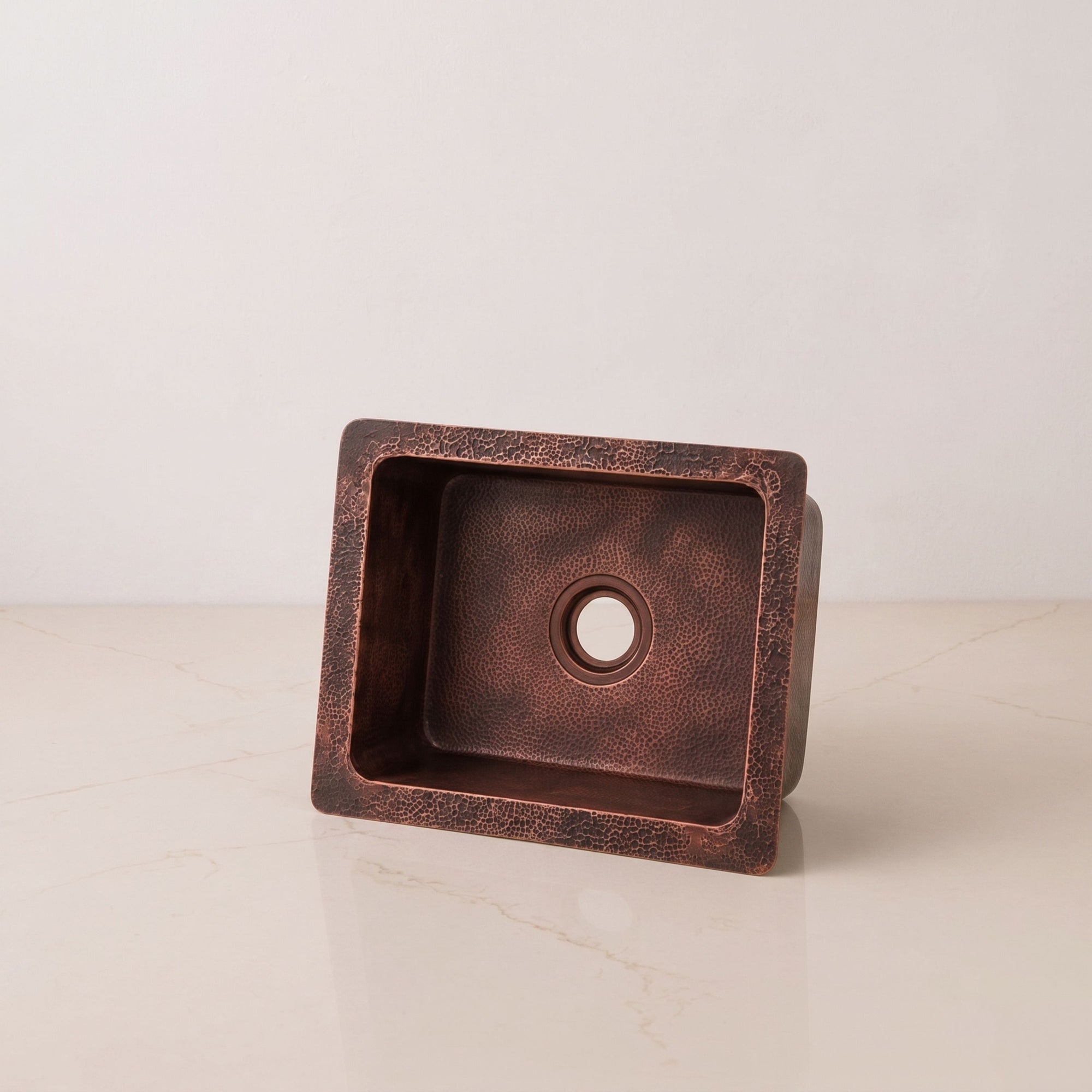 A high-quality image of an artisanal hammered copper sink, highlighting its warm coppery-bronze color and square design, perfect for adding a rustic touch to a kitchen or bar.