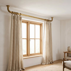 curtains hanging from a brass curtain rod in a room with a wooden window frame.