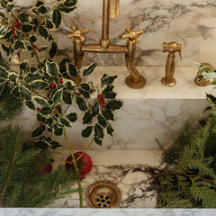 Decorative bathroom sink with gold fixtures and greenery on a marble countertop.