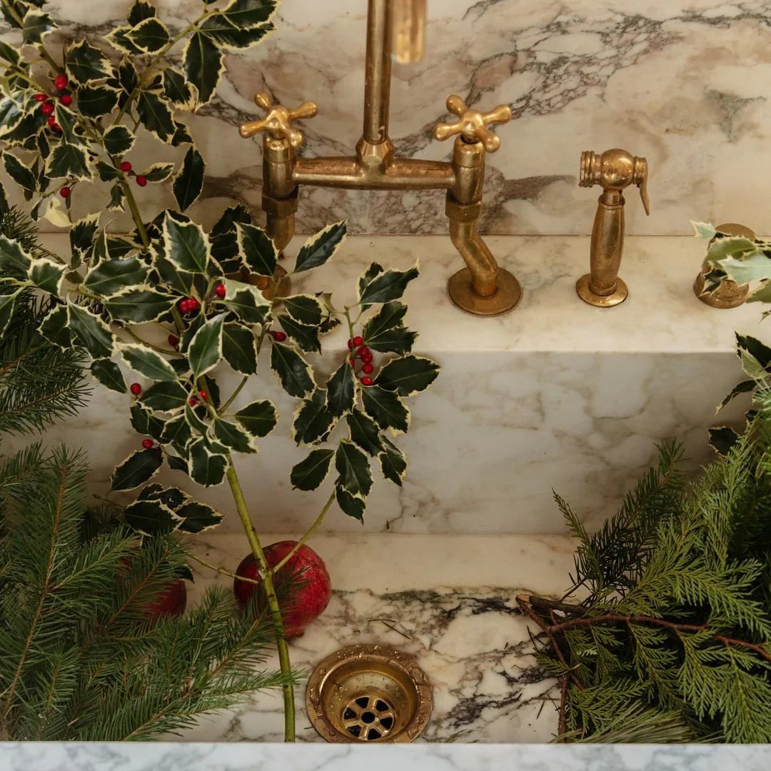 Decorative bathroom sink with gold fixtures and greenery on a marble countertop.