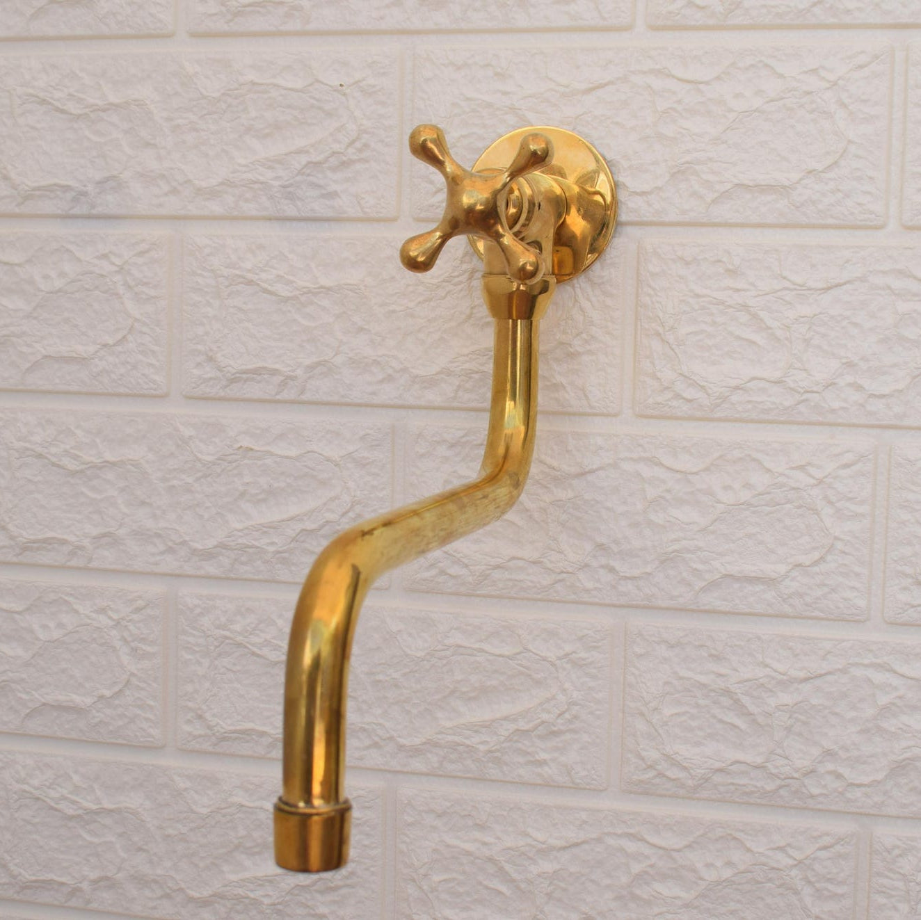 A polished brass wall-mounted faucet spout with a cross-handle valve