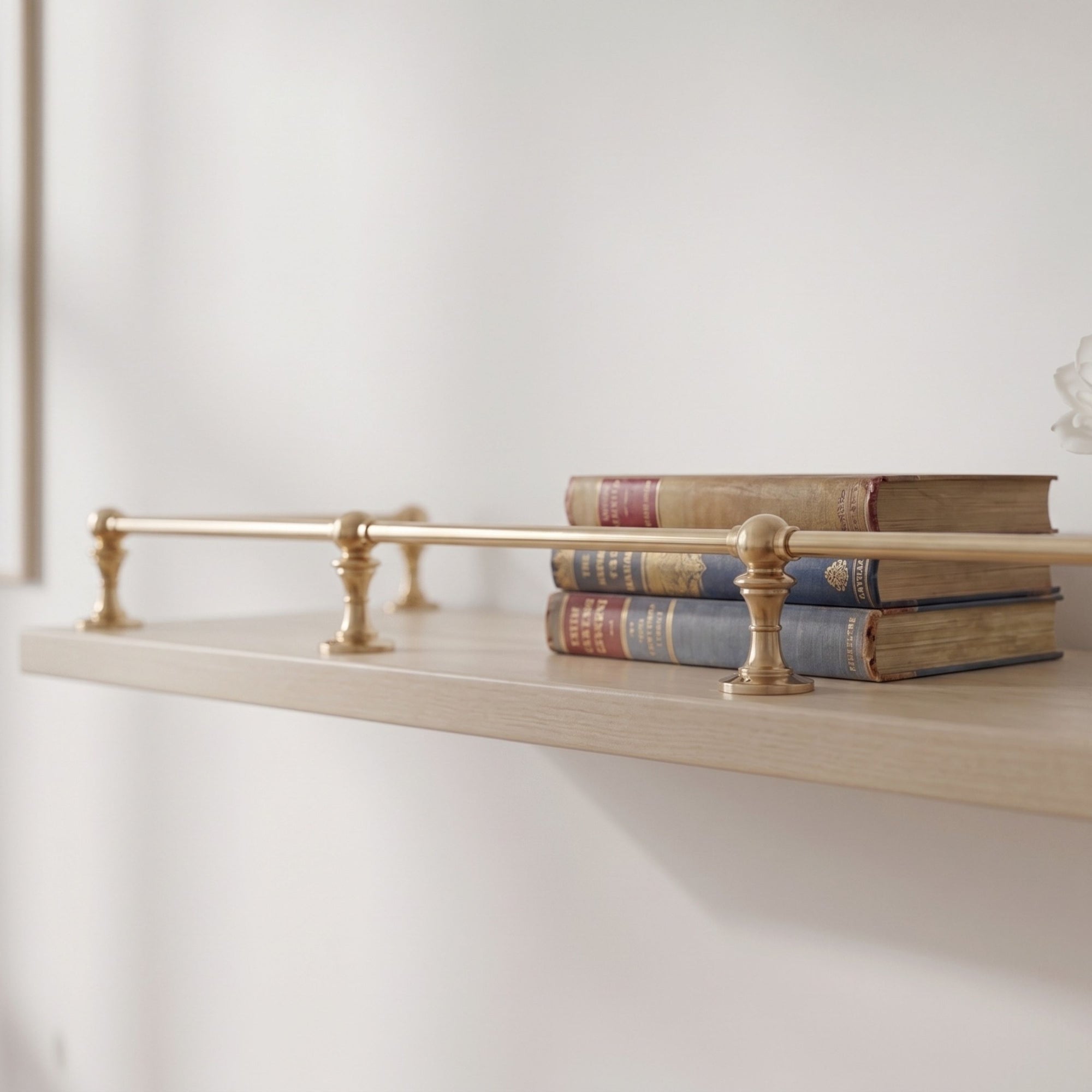 Front view of a handcrafted solid brass gallery rail mounted on a modern minimalist white-beige wooden shelf, showing the end posts and center supporting posts.