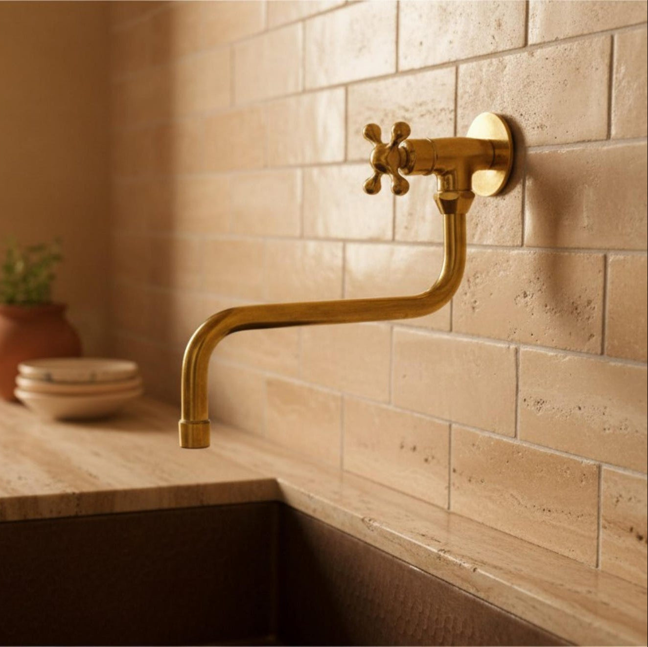 A wall-mounted brass faucet with a cross handle and curved spout