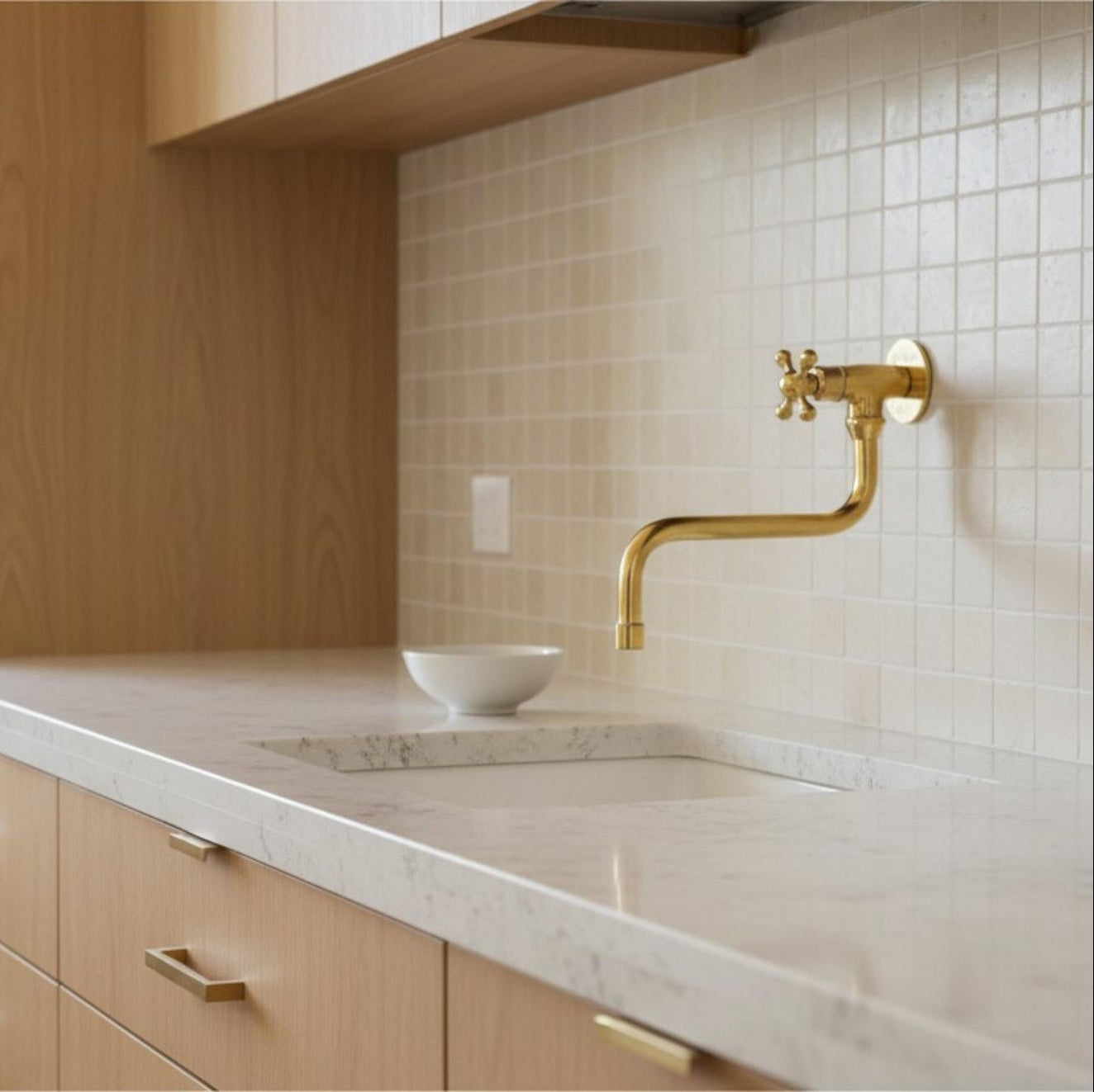 polished brass wall-mounted faucet with a single cross handle.