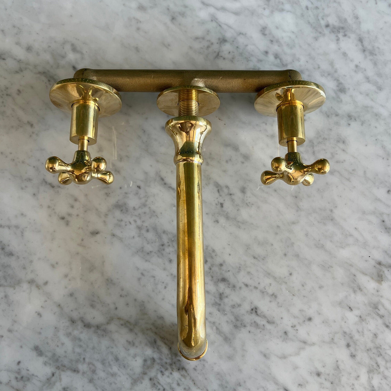 A polished brass three-hole faucet set with a central spout and two cross-handle valves, shown on a white and gray marble surface.