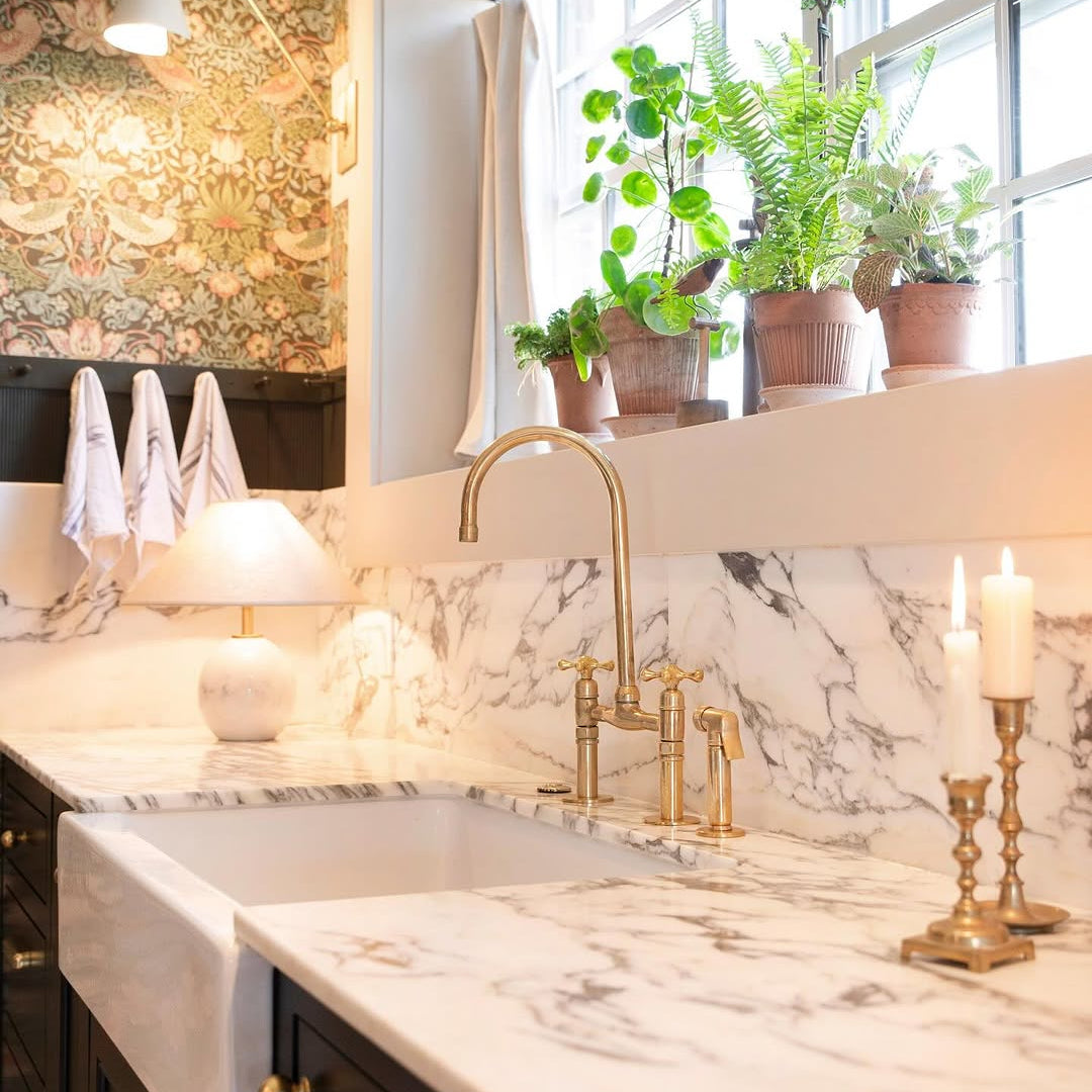 Modern kitchen with marble countertop, gold faucet, and decorative elements.
