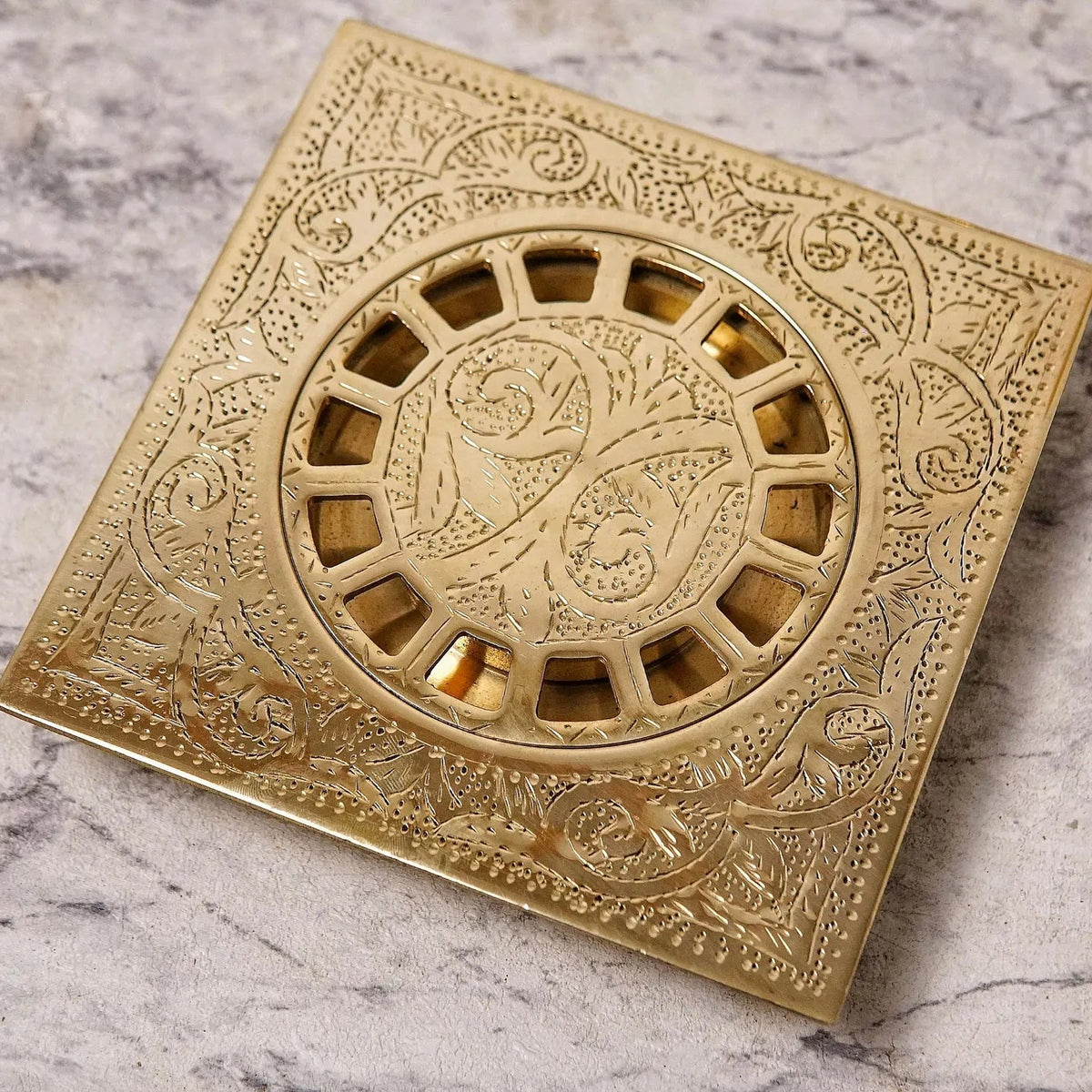 An engraved brass square shower drain with a geometric pattern.