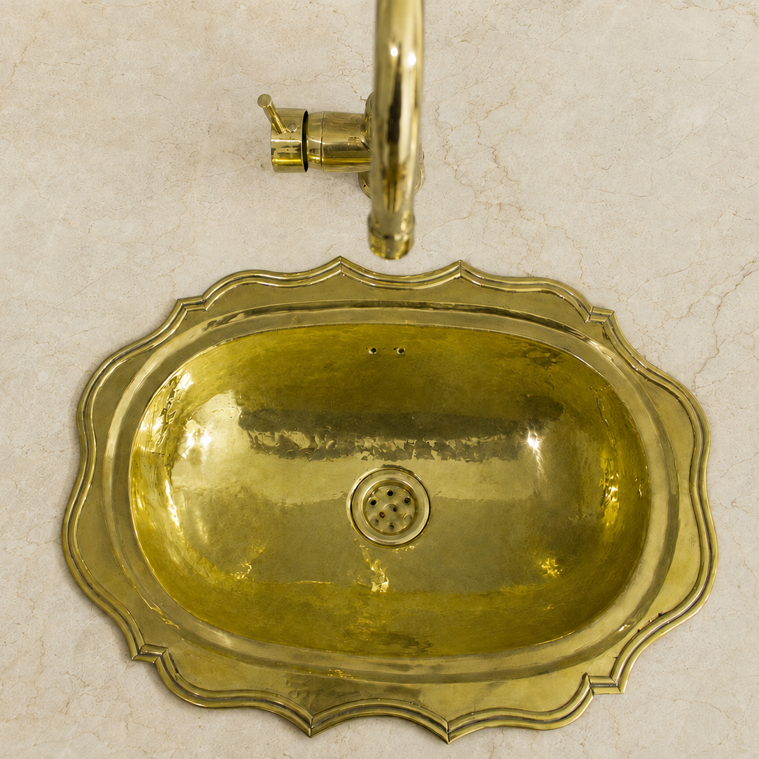 A decorative oval brass sink with a matching curved faucet, shown against a light beige marble background.
