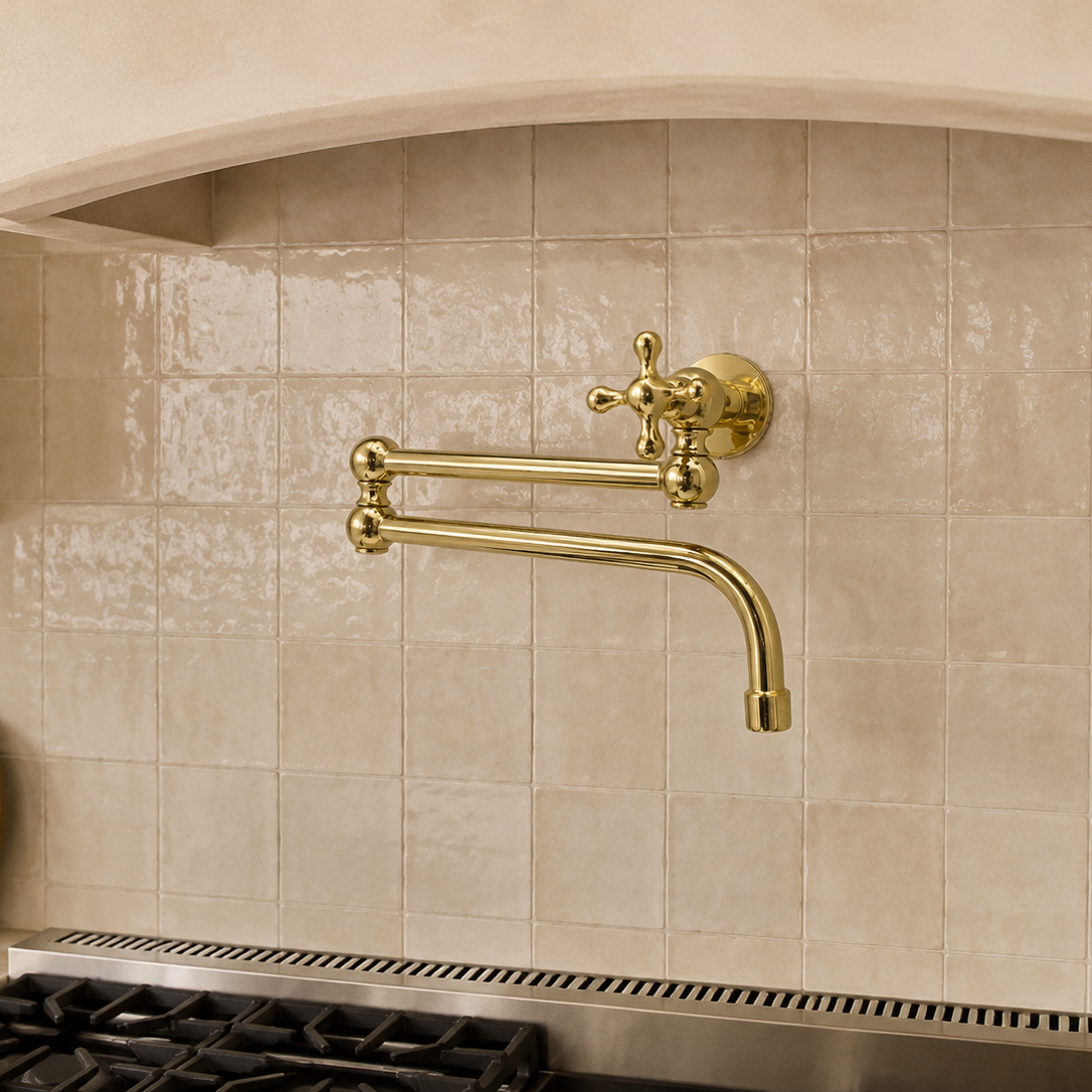 A wall-mounted kitchen faucet with two curved brass-style handles and a curved spout, installed against a beige tiled backsplash above a gas stove.