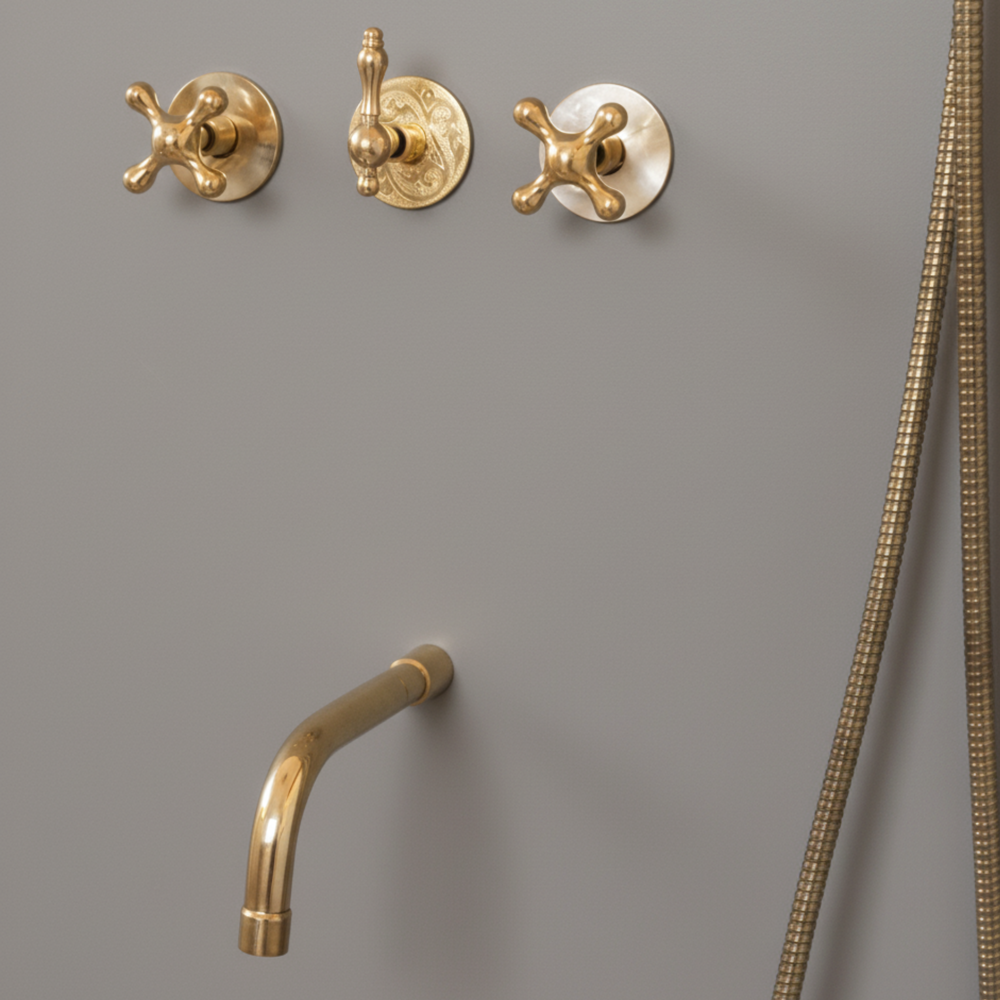 Brass bathroom fixtures including a shower head and control handles on a gray wall.
